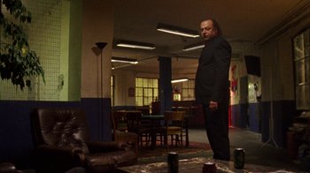 Movie still from “Pusher III” (2005), directed by Nicolas Winding Refn – A man in a suit standing in a living room; Wide shot, Low angle