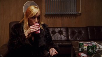 Movie still from “Pusher III” (2005), directed by Nicolas Winding Refn – A woman sitting at a table drinking a beverage; Medium shot, Over the shoulder angle