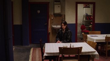 Movie still from “Pusher III” (2005), directed by Nicolas Winding Refn – A woman sitting at a table in front of a door; Wide shot, High angle