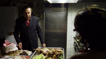 Movie still from “Pusher III” (2005), directed by Nicolas Winding Refn – A man standing in front of a tray of food in a kitchen; Medium shot, Over the shoulder angle
