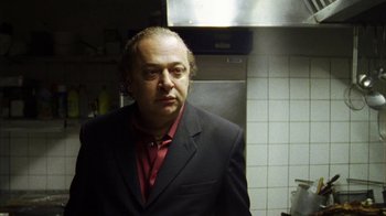 Movie still from “Pusher III” (2005), directed by Nicolas Winding Refn – A man in a suit and red shirt in a kitchen; Close Up shot, Low angle