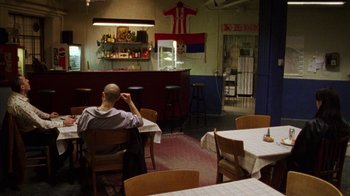 Movie still from “Pusher III” (2005), directed by Nicolas Winding Refn – A man sitting at a table in front of a bar; Wide shot, Over the shoulder angle