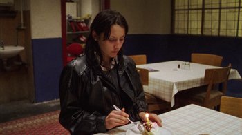 Movie still from “Pusher III” (2005), directed by Nicolas Winding Refn – A woman sitting at a table with a lit candle in front of a cake; Medium shot, High angle