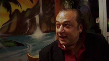 Movie still from “Pusher III” (2005), directed by Nicolas Winding Refn – A person sitting in a chair wearing a suit; Close Up shot, Low angle