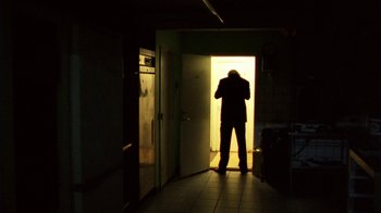 Movie still from “Pusher III” (2005), directed by Nicolas Winding Refn – A man standing in a doorway in the dark; Wide shot, Low angle