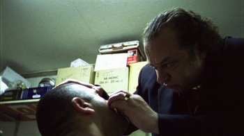 Movie still from “Pusher III” (2005), directed by Nicolas Winding Refn – A man getting his head shaved by another man; Close Up shot, Low angle