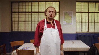 Movie still from “Pusher III” (2005), directed by Nicolas Winding Refn – An older man wearing an apron standing in front of a table; Medium shot, Low angle