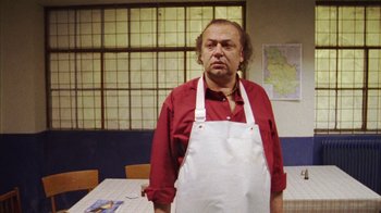 Movie still from “Pusher III” (2005), directed by Nicolas Winding Refn – A man wearing an apron standing in front of a table; Medium shot, Low angle