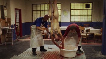 Movie still from “Pusher III” (2005), directed by Nicolas Winding Refn – Three men in aprons are hanging upside down; Wide shot, Overhead angle