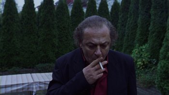 Movie still from “Pusher III” (2005), directed by Nicolas Winding Refn – A man smoking a cigarette in front of some trees; Medium shot, Low angle