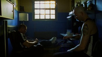 Movie still from “Pusher II” (2004), directed by Nicolas Winding Refn – Two men sitting on a couch in front of a window; Wide shot, High angle