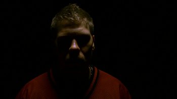 Movie still from “Pusher II” (2004), directed by Nicolas Winding Refn – A man in a red shirt is in the dark; Extreme Close Up shot, Low angle