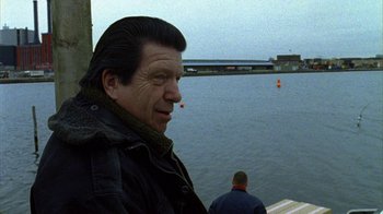 Movie still from “Pusher II” (2004), directed by Nicolas Winding Refn – A man standing next to a body of water; Medium shot, Over the shoulder angle