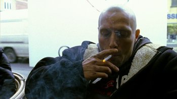 Movie still from “Pusher II” (2004), directed by Nicolas Winding Refn – A man smoking a cigarette while sitting on a bench; Close Up shot, Low angle