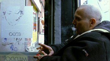 Movie still from “Pusher II” (2004), directed by Nicolas Winding Refn – A man smoking a cigarette while sitting on a bench; Close Up shot, Over the shoulder angle