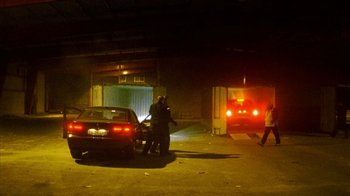 Movie still from “Pusher II” (2004), directed by Nicolas Winding Refn – Two men standing next to a car in a garage; Extreme Wide shot, Low angle
