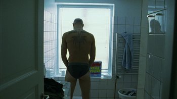 Movie still from “Pusher II” (2004), directed by Nicolas Winding Refn – A man standing in front of a window in a bathroom; Medium shot, Low angle