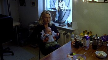 Movie still from “Pusher II” (2004), directed by Nicolas Winding Refn – A woman sitting in a chair holding a baby in her arms; Medium shot, High angle