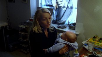 Movie still from “Pusher II” (2004), directed by Nicolas Winding Refn – A woman holding a baby in her arms in front of a window; Medium shot, High angle