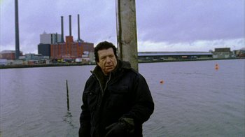 Movie still from “Pusher II” (2004), directed by Nicolas Winding Refn – A man standing in front of a body of water; Medium shot, Low angle