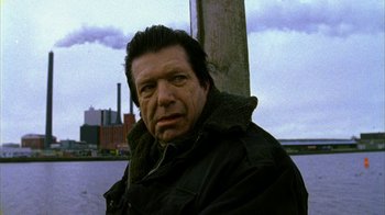 Movie still from “Pusher II” (2004), directed by Nicolas Winding Refn – A person wearing a jacket near a pole; Close Up shot, Low angle