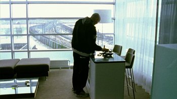 Movie still from “Pusher II” (2004), directed by Nicolas Winding Refn – A man standing in front of a counter in front of a window; Wide shot, Low angle