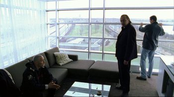 Movie still from “Pusher II” (2004), directed by Nicolas Winding Refn – Two men in a living room with a large window; Wide shot, Over the shoulder angle