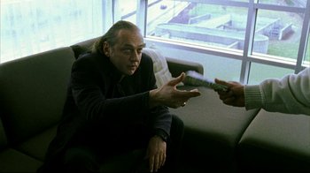 Movie still from “Pusher II” (2004), directed by Nicolas Winding Refn – A man sitting on a couch talking to another man; Medium shot, Over the shoulder angle