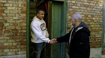 Movie still from “Pusher II” (2004), directed by Nicolas Winding Refn – Two men shaking hands in front of a building; Medium shot, Over the shoulder angle