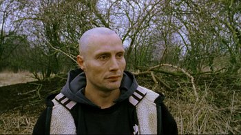 Movie still from “Pusher II” (2004), directed by Nicolas Winding Refn – A man with a bald head is standing in a wooded area; Close Up shot, Low angle