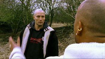 Movie still from “Pusher II” (2004), directed by Nicolas Winding Refn – A bald man in a black shirt is talking to another man; Close Up shot, Over the shoulder angle