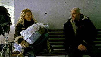 Movie still from “Pusher II” (2004), directed by Nicolas Winding Refn – Two people sitting on a wooden bench with a blanket; Medium shot, High angle