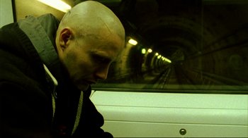 Movie still from “Pusher II” (2004), directed by Nicolas Winding Refn – A man with a bald head riding in a subway car; Close Up shot, Low angle