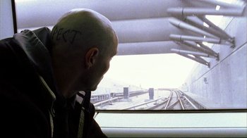 Movie still from “Pusher II” (2004), directed by Nicolas Winding Refn – A bald man sitting in front of a train window; Close Up shot, Over the shoulder angle