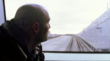 Movie still from “Pusher II” (2004), directed by Nicolas Winding Refn – A man looking out of a train window at a train track; Close Up shot, Low angle