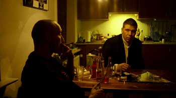 Movie still from “Pusher II” (2004), directed by Nicolas Winding Refn – Two men are sitting at a table with drinks; Medium shot, Low angle