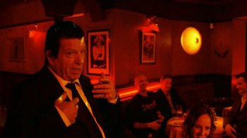 Movie still from “Pusher II” (2004), directed by Nicolas Winding Refn – A group of people sitting in a room with drinks; Medium shot, Over the shoulder angle