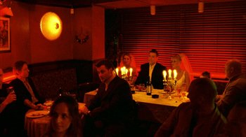 Movie still from “Pusher II” (2004), directed by Nicolas Winding Refn – A group of people sitting around a table with candles; Wide shot, Low angle