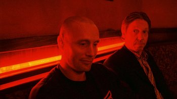 Movie still from “Pusher II” (2004), directed by Nicolas Winding Refn – A man with a shaved head sitting next to another man; Close Up shot, Low angle
