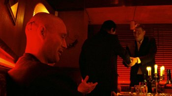 Movie still from “Pusher II” (2004), directed by Nicolas Winding Refn – A man in a black shirt is talking to another man in a black suit; Medium shot, Over the shoulder angle