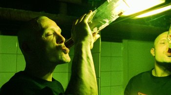 Movie still from “Pusher II” (2004), directed by Nicolas Winding Refn – A man is drinking from a bottle in a green light; Close Up shot, Low angle