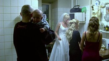 Movie still from “Pusher II” (2004), directed by Nicolas Winding Refn – A man holding a baby in his arms while a woman in a wedding dress holds a veil over her head; Medium shot, Over the shoulder angle