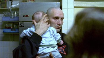 Movie still from “Pusher II” (2004), directed by Nicolas Winding Refn – A man holding a baby in his arms in front of a mirror; Close Up shot, Over the shoulder angle