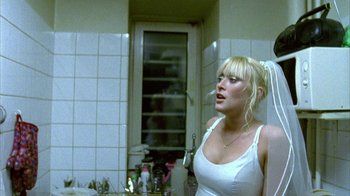 Movie still from “Pusher II” (2004), directed by Nicolas Winding Refn – A woman standing in a kitchen next to a sink; Medium shot, Over the shoulder angle