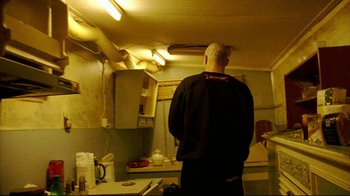 Movie still from “Pusher II” (2004), directed by Nicolas Winding Refn – A man standing in a kitchen looking into a sink; Medium shot, Low angle
