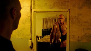 Movie still from “Pusher II” (2004), directed by Nicolas Winding Refn – A man holding a knife standing in front of an open door; Medium shot, Low angle