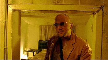 Movie still from “Pusher II” (2004), directed by Nicolas Winding Refn – A bald man with glasses is standing in a room; Close Up shot, Low angle
