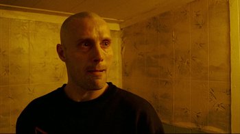 Movie still from “Pusher II” (2004), directed by Nicolas Winding Refn – A man with a bald head looking into the camera; Close Up shot, Low angle