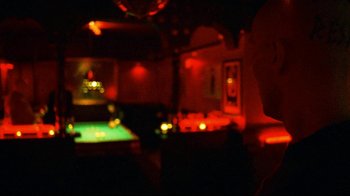 Movie still from “Pusher II” (2004), directed by Nicolas Winding Refn – A man sitting at a pool table in a dark room; Close Up shot, Over the shoulder angle