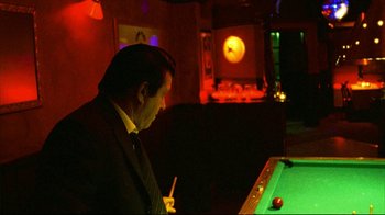 Movie still from “Pusher II” (2004), directed by Nicolas Winding Refn – A man in a black suit playing a game of billiards; Medium shot, Over the shoulder angle